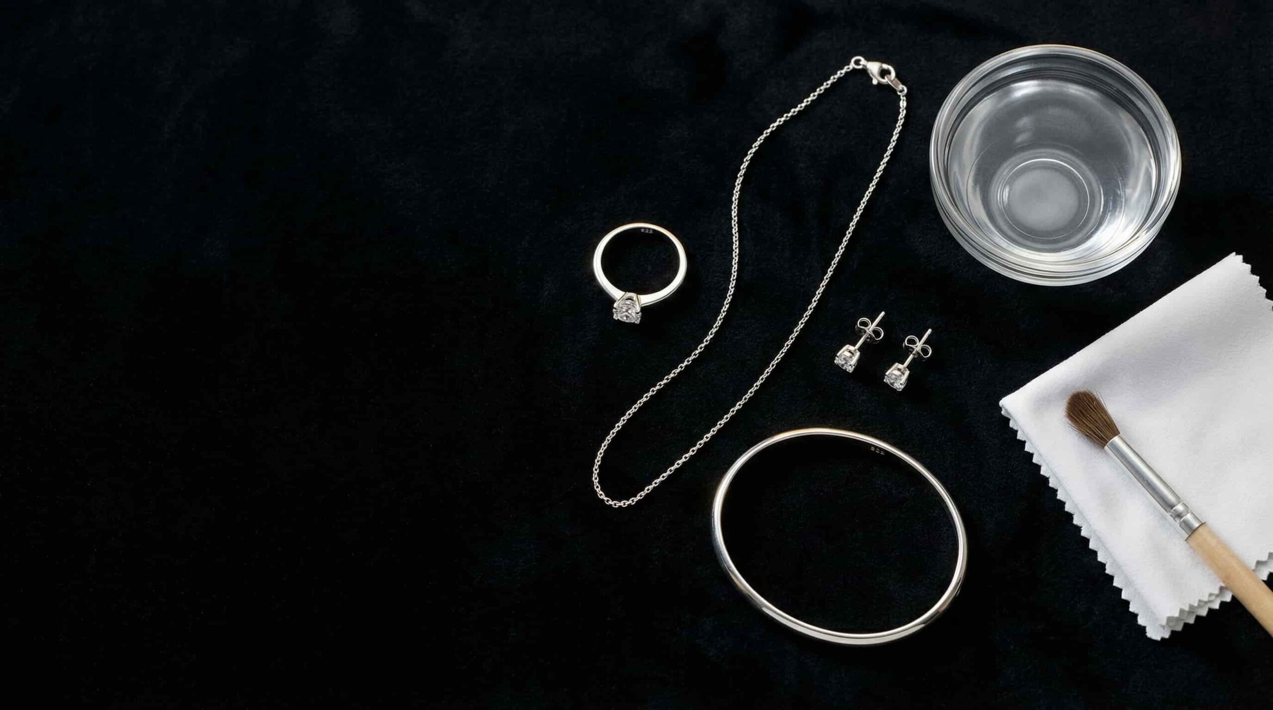 925 sterling silver ring, necklace, earrings, and bangle arranged on black velvet with a white microfibre cloth and soft brush for jewellery care